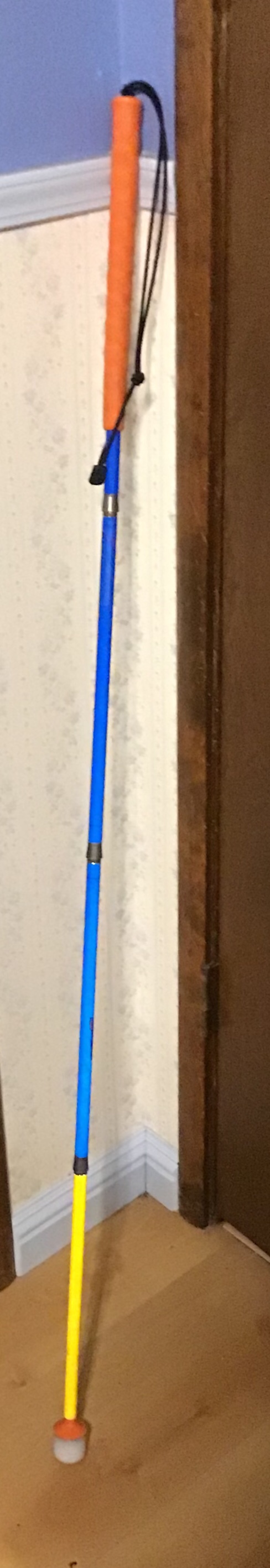 An orange, blue, and yellow cane leaning against a wall that is white on the bottom and blue on the top.